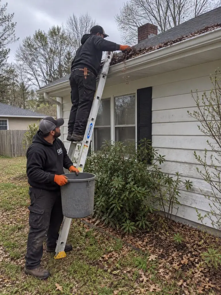 Two GMX crew members clearing a gutter from a ladder with a debris bucket in Milford, MA