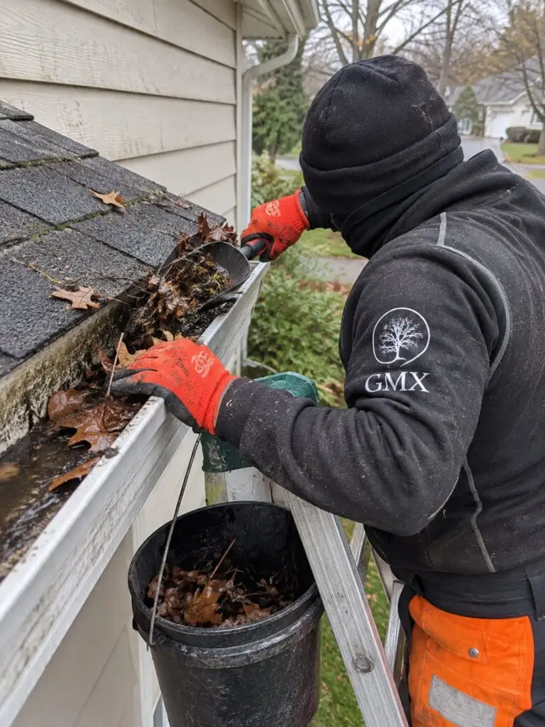 GMX crew member scooping gutter debris into a hanging bucket in Milford, MA