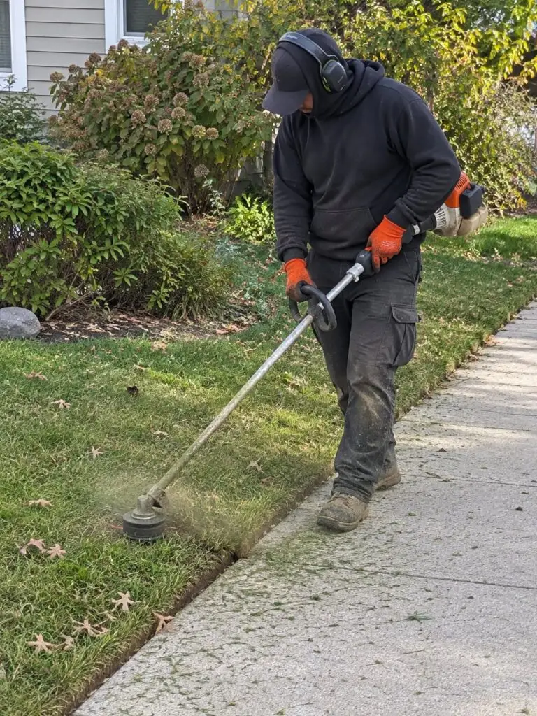 GMX crew member edging along a sidewalk with a string trimmer in Milford, MA