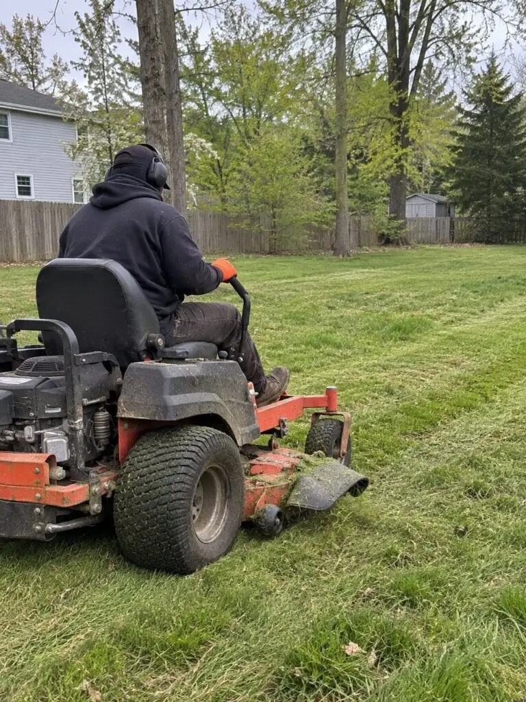 GMX operator mowing a large backyard with a zero-turn riding mower in Milford, MA